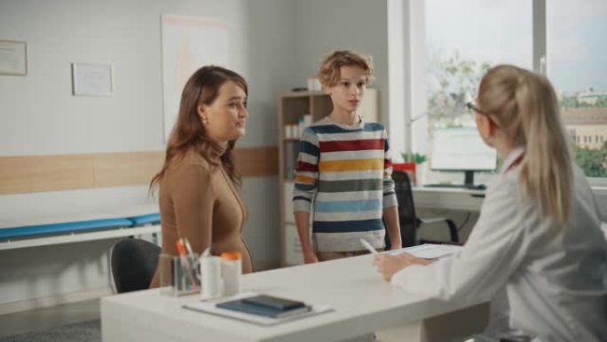 女家庭医生与年轻的孕妇和她的十几岁的男孩在一个诊所咨询。穿着白大褂的经验丰富的医生坐在医院办公室的电