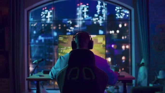 在家里霓虹灯照明的客厅中，一名非裔美国人游戏玩家在个人电脑上的视频游戏中获胜。阁楼公寓舒适的夜晚。