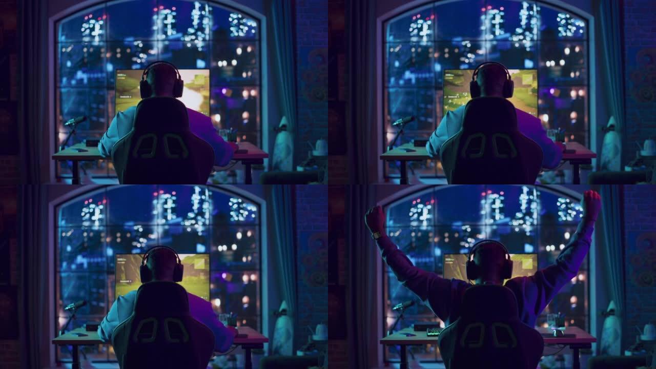 在家里霓虹灯照明的客厅中，一名非裔美国人游戏玩家在个人电脑上的视频游戏中获胜。阁楼公寓舒适的夜晚。