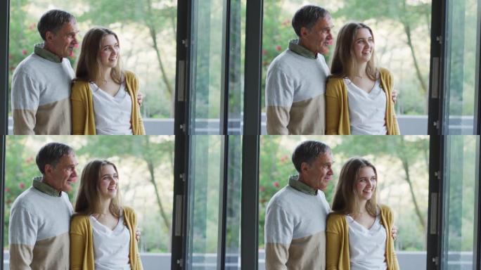 微笑的白人高级父亲和十几岁的女儿拥抱并看着窗外