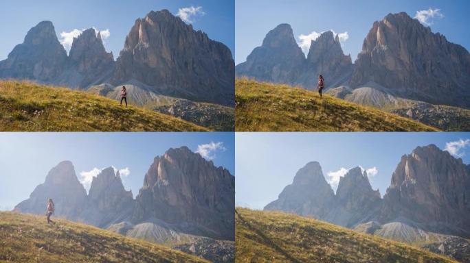 女人很活跃，在雄伟的山脉前的草地上爬山