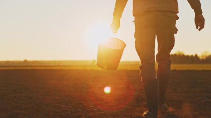 农民在日落时分穿越田野时拿着水桶