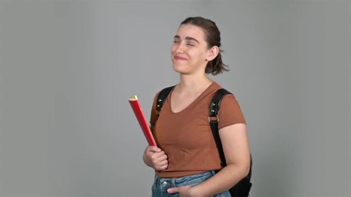 视频中灰色背景前拿着笔记本的年轻女孩。与黑色背包合影。