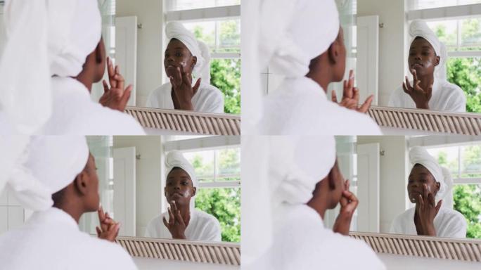 穿着浴袍的非裔美国妇女在家照镜子时涂面霜
