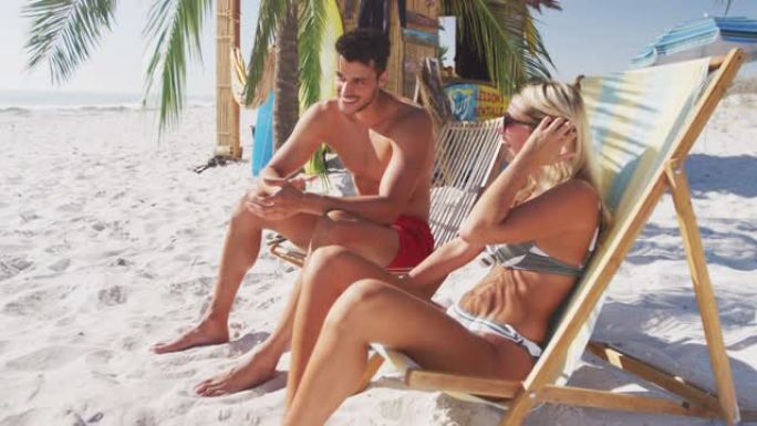 白人夫妇坐在沙滩上的日光浴床上