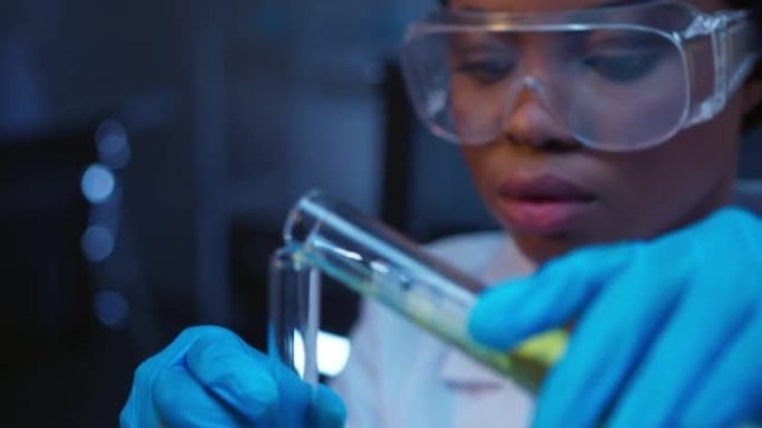 一位年轻的深色皮肤化学家戴着防护眼镜和一件实验室外套，用绿色液体在玻璃试管中进行化学反应