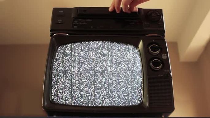 男性手将VHS放入VCR和一台带有绿色屏幕的旧电视。