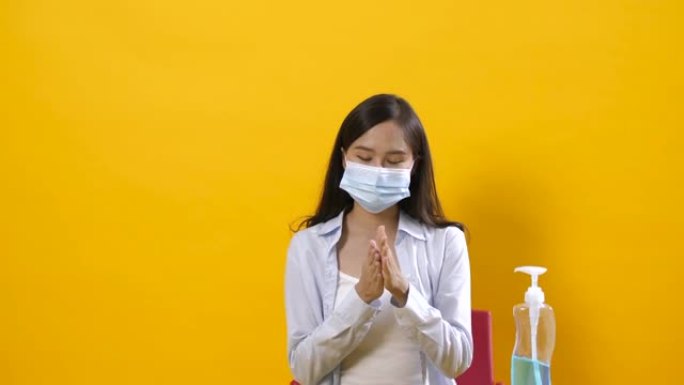 美丽的亚洲女人戴上防护医用口罩，在工作室黄色背景下洗手