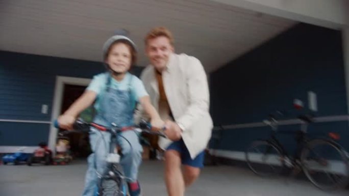 开朗的父亲教女儿在他们美丽的住宅区家前院骑自行车。戴头盔的女孩，勇敢地在自行车上平衡自己。手持镜头。