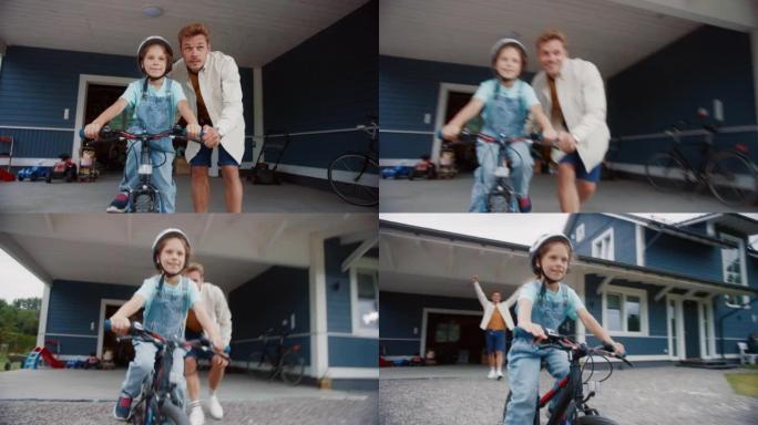 开朗的父亲教女儿在他们美丽的住宅区家前院骑自行车。戴头盔的女孩，勇敢地在自行车上平衡自己。手持镜头。