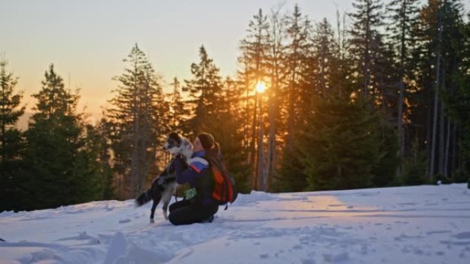 SLO MO女人在日出时在雪坡上拥抱她的狗
