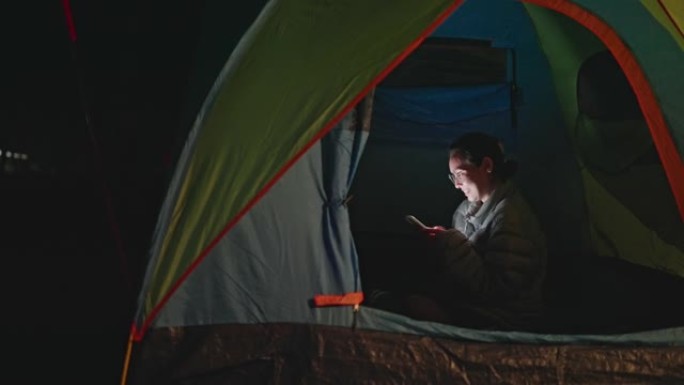 露营时，亚洲妇女晚上在帐篷里使用手机