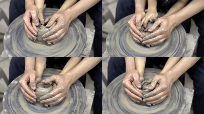 一个年轻的妈妈和她的孩子的特写手在陶轮上塑造粘土。