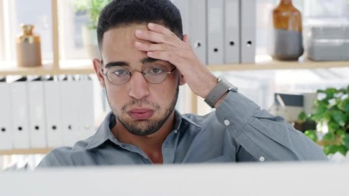 4k视频片段，一个英俊的年轻商人独自坐在办公室里，在使用计算机时感到压力