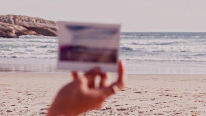 夏天，在海边的沙滩上，用女人的手在户外的沙滩上旅行和拍照。海洋，自然和宝丽来，女性在度假或度假时拿着