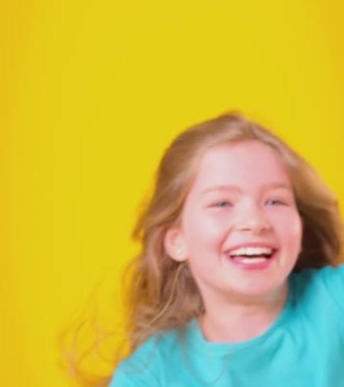 长发女孩旋转并在黄色背景下大笑的垂直视频-慢动作拍摄