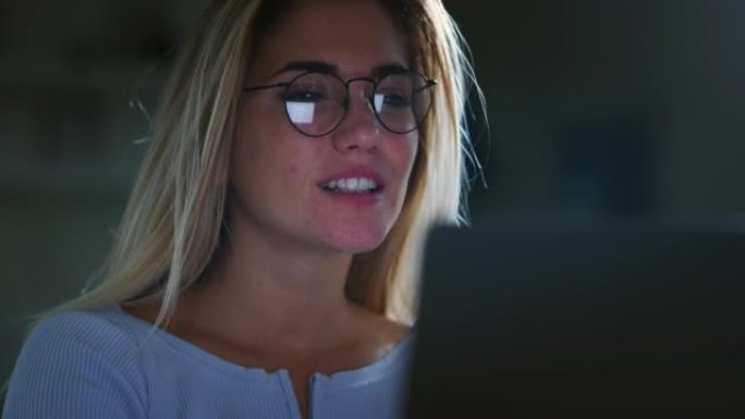 一位年轻成功的女商人戴着眼镜的真实照片，晚上在办公室里用电脑工作时，她对自己的工作感到满意。