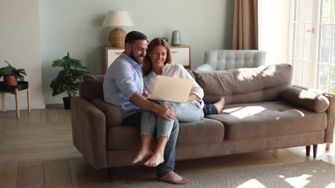 结合年轻的配偶拥抱在笔记本电脑屏幕上的沙发上