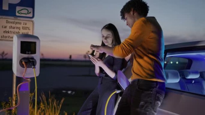 SLO MO年轻夫妇在晚上为电动汽车充电时使用智能手机