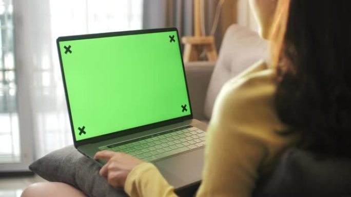 女人坐在沙发上看着绿色屏幕的笔记本电脑