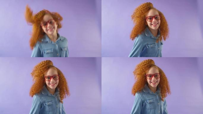在紫色工作室背景下，红头发和眼镜的微笑女孩跳进框架的工作室镜头-慢动作拍摄