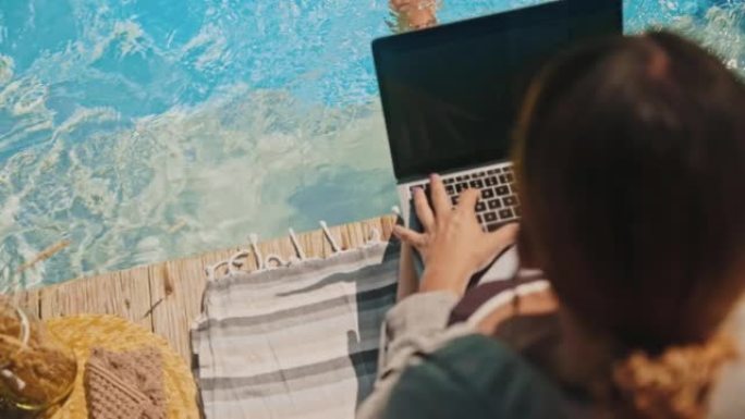 SLO MO女人坐在游泳池边缘时使用笔记本电脑