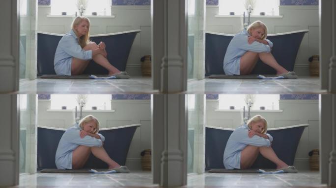 患有失禁的更年期成熟妇女坐在浴室的地板上拿着失禁垫-慢动作射击