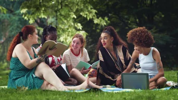 各种各样的女性朋友讨论和使用笔记本电脑。一群多种族的女学生在户外大学项目中工作，并享受夏季的好天气