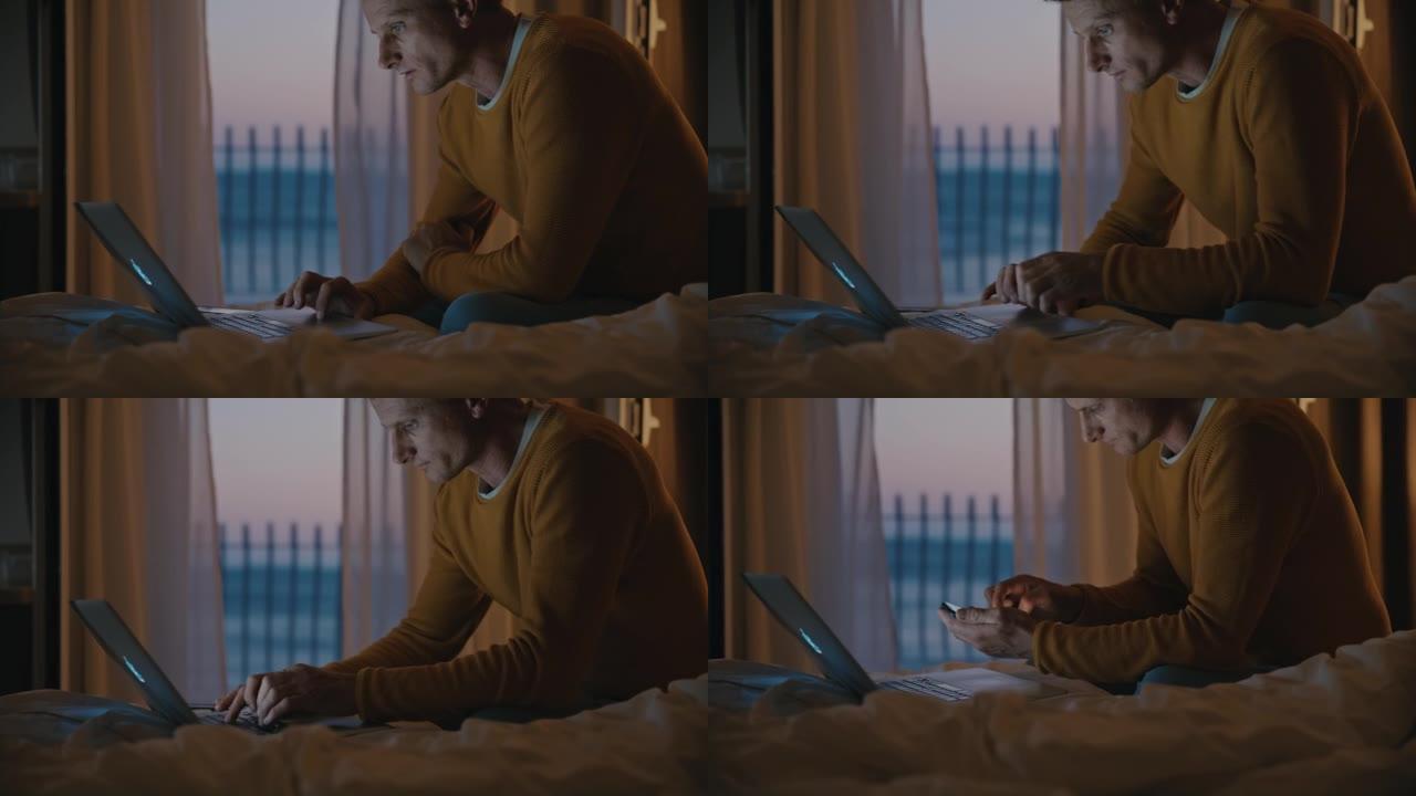 晚上，棕色短发的男人在笔记本电脑上工作，坐在酒店房间的床上，背景是阳台和大海，使用智能手机