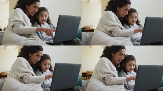 快乐的混血母女坐在沙发上，玩得开心，用笔记本电脑