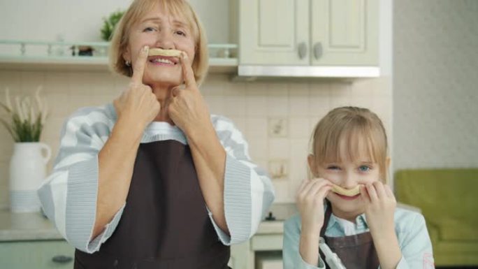 小女孩和顽皮的奶奶在厨房里留着面团胡子的肖像