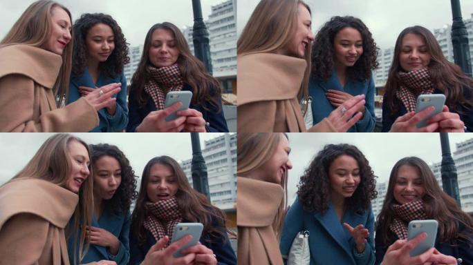 社交网络概念。在寒冷的阴天使用智能手机应用程序的特写美丽的年轻快乐多样化的女性朋友。