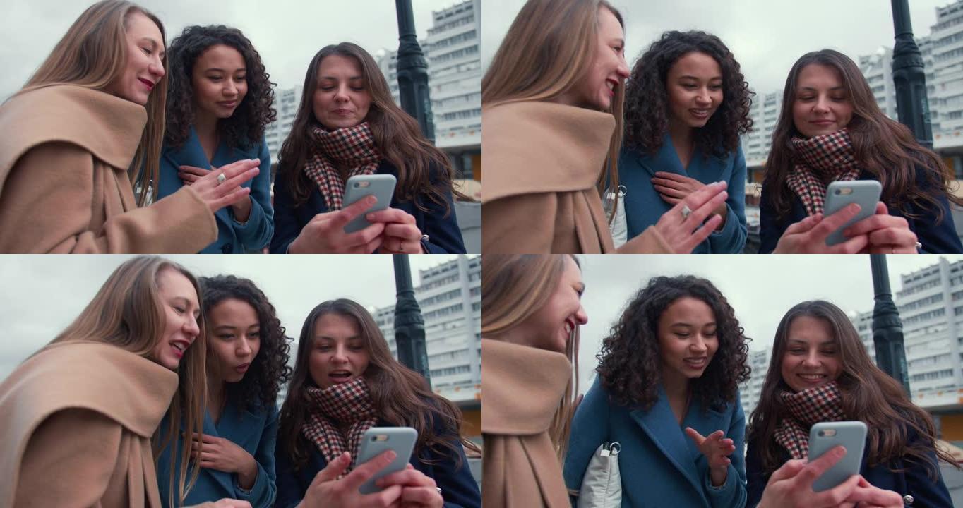 社交网络概念。在寒冷的阴天使用智能手机应用程序的特写美丽的年轻快乐多样化的女性朋友。