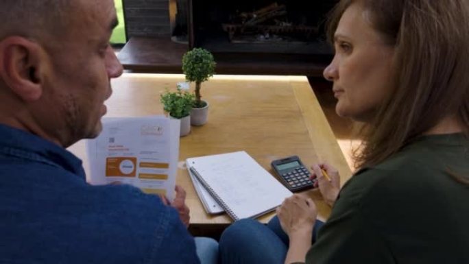 成熟的异性恋夫妇在家中计划自己的财务状况，同时使用笔记本，笔和计算器查看水电费