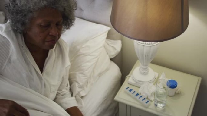 生病的非裔美国高级妇女喝水躺在家里的床上