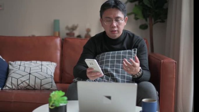 中年中国成年人在家工作，带笔记本电脑坐在沙发客厅，带笔记本电脑和智能手机