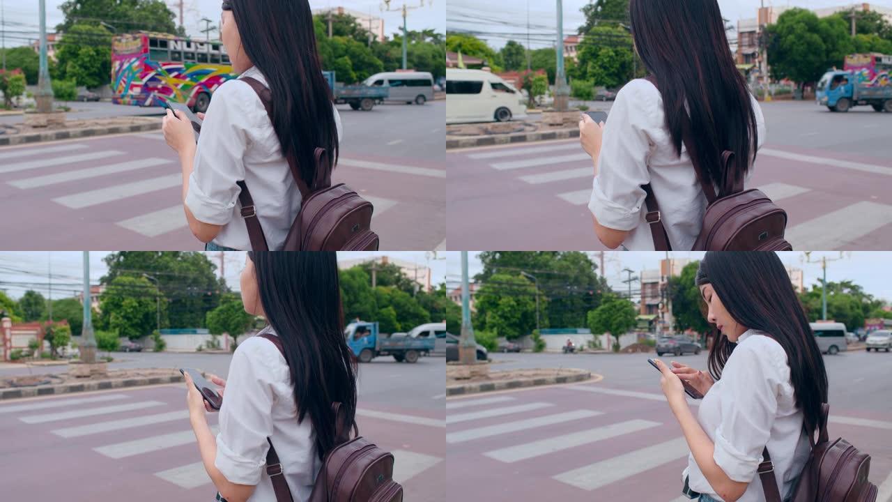 年轻的亚洲背包客女游客用相机站在十字路口街前看手机搜索导航应用的位置。