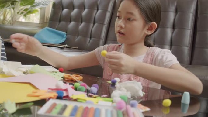 亚洲女孩在家时在客厅剪纸并制作手工艺品。他们使用彩纸，剪刀和胶水在纸上创作艺术作品，以形成她的想象力