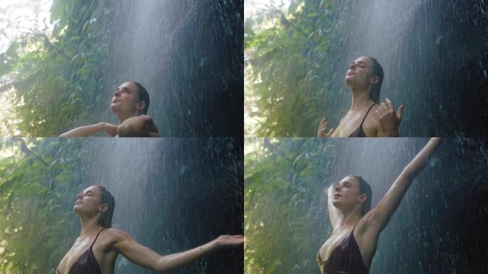 穿着性感比基尼的瀑布下旅行女人享受热带丛林4k中清新的水溅到身上的乐趣