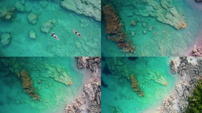 情侣在透明的绿松石海水中游泳的鸟瞰图，相机升起。在僻静的海湾的海滩上放暑假。人们在海上暑假。旅行，放