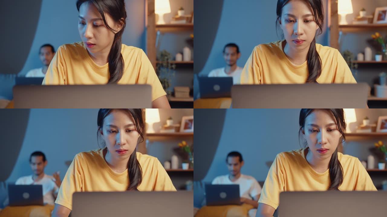 自由职业者亚洲夫妇在休闲丈夫的焦点工作在笔记本电脑晚上妻子休息一下，感觉放松戴耳机在智能手机上播放音