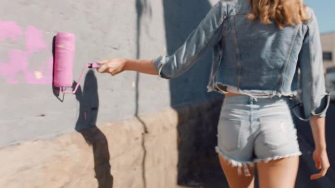 美丽的艺术家女人用粉色油漆画墙走在城市街道上自信叛逆的女性享受城市涂鸦艺术表达