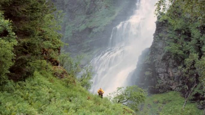 4k视频片段，一个无法识别的女人站着并用手机拍摄挪威瀑布的照片