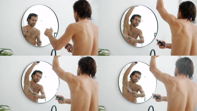 英俊的年轻人在浴室使用除臭喷雾在腋窝上照镜子