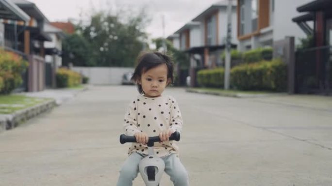 快乐的亚洲小女孩骑着蹒跚学步的踏板车。