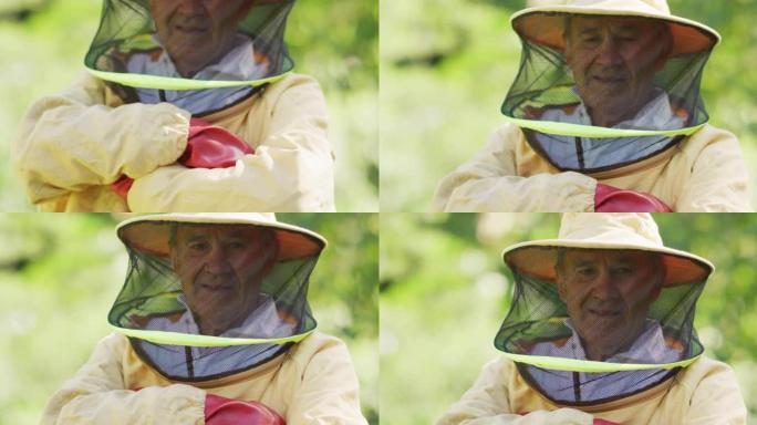 微笑的白人男性养蜂人的肖像，穿着双臂交叉的防护服