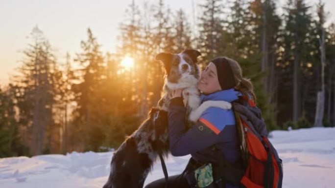 SLO MO女人和她的狗在日出时在雪坡上拥抱