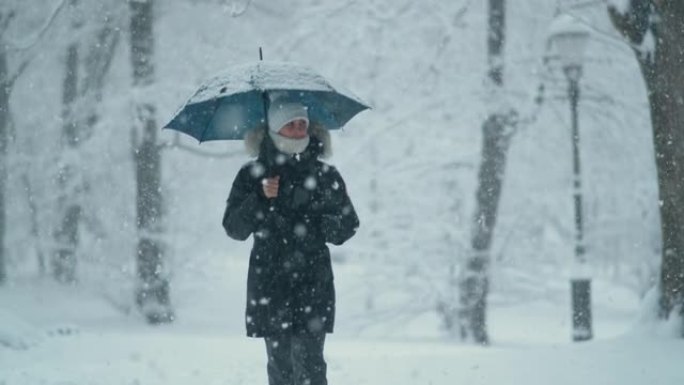 特写: 一场暴风雪中，穿着厚厚的冬衣的年轻女子沿着大街走