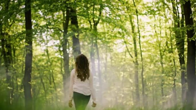 SLO MO女人在阳光明媚的森林中张开双臂奔跑