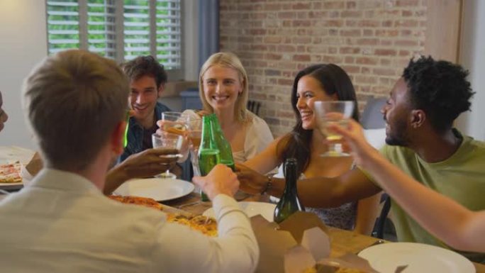 多元文化的朋友在一起在家享受啤酒和披萨派对时敬酒